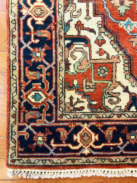 Detail of a colorful, intricate Persian rug featuring rich reds, blues, and cream with ornate patterns and a fringed edge.